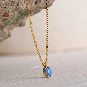 Gold necklace with a blue pendant on a stone surface