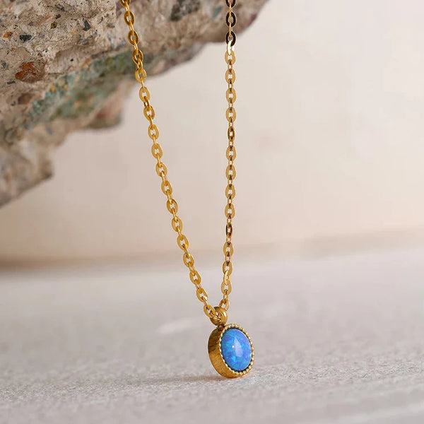 Gold necklace with a blue pendant on a stone surface