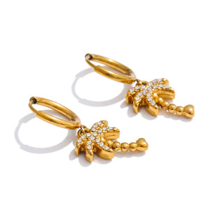 A pair of gold huggie hoop earrings with dangling palm tree charms embellished with clear crystals, shown on a clean white background with soft shadows.