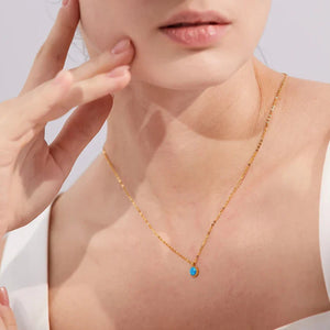 Close-up of a person wearing a gold necklace with a blue gemstone on a light background