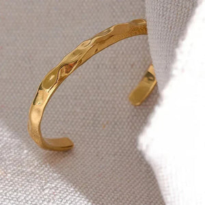 Hammered 18K gold-plated cuff bracelet on neutral textured fabric background