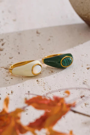 Two rings, one gold and one green, on a textured surface with dried leaves.