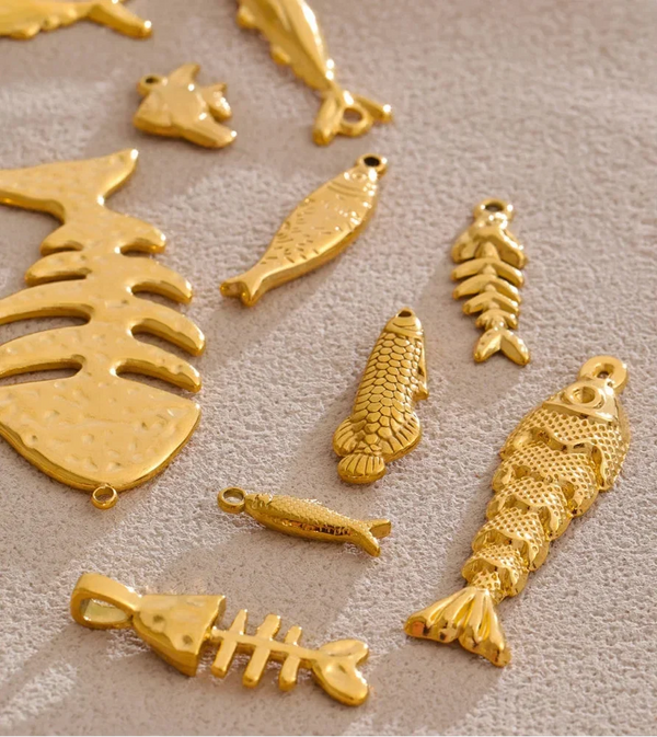 A set of gold-colored fish and fish skeleton charms with textured details, arranged on a neutral beige textured background.