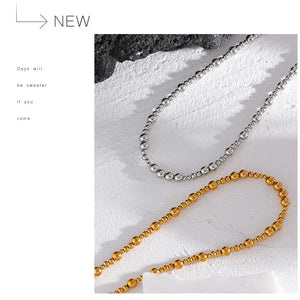Two necklaces, one silver and one gold, on a textured white surface with 'NEW' text.