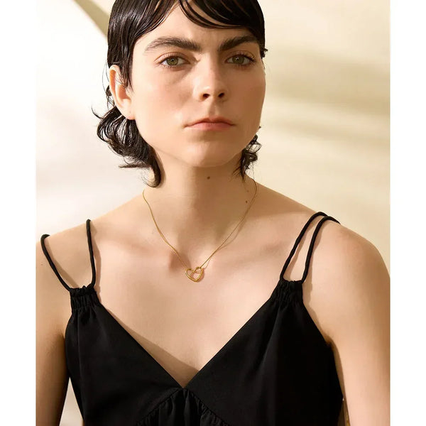 Woman wearing a gold-plated heart pendant necklace with a black spaghetti strap dress