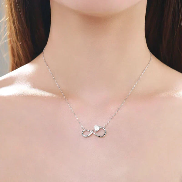 Silver infinity necklace with a heart detail on a model's neck.Glowing Heart Charm Necklace - TM & CO. JEWELS 