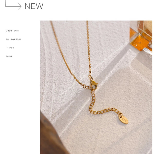 Gold necklace on a textured white surface with 'NEW' text above.