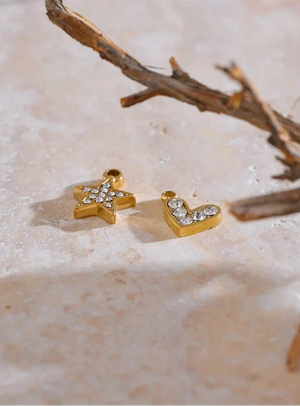 Gold star and letter 'L' charms on a textured surface with a branch in the background