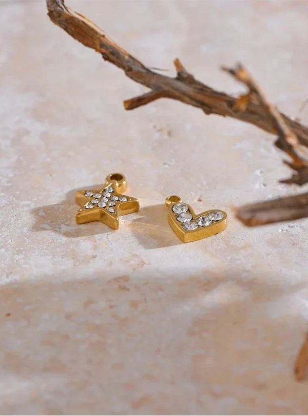 Gold star and letter 'L' charms on a textured surface with a branch in the background