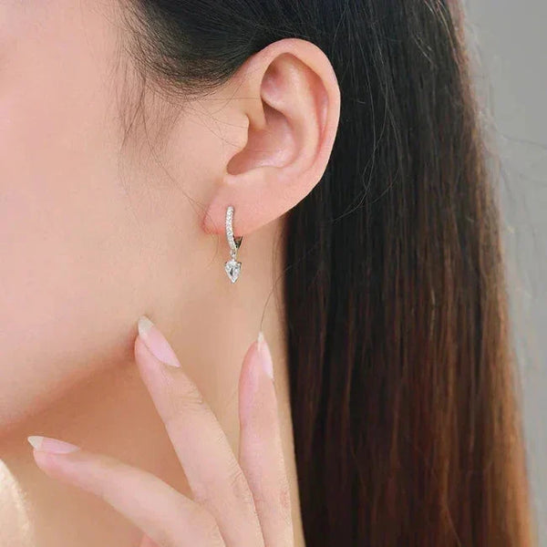 Close-up of a woman wearing Sparkling Hoop Earrings - TM & CO. JEWELS - a silver hoop earring with a heart-shaped gemstone.