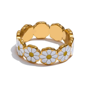 A gold-plated stretch band ring decorated with white enamel daisy flowers with yellow centers, shown on a clean white background.