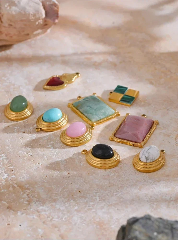 Collection of gold-framed gemstone pendants on a textured beige surface
