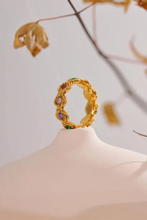Gold ring with colorful gemstones on a mannequin head against a neutral background
