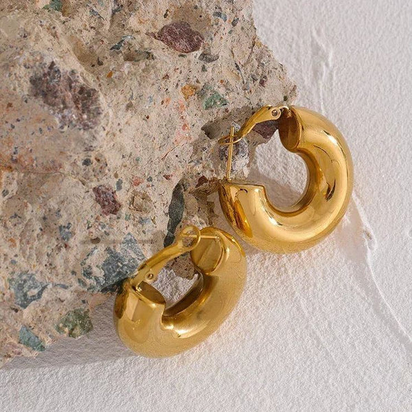 Chunky 18K gold-plated hoop earrings on textured stone background