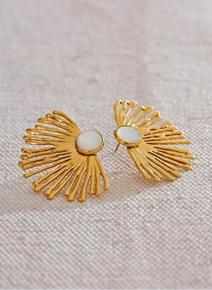 Gold earrings with a central gemstone on a textured beige background