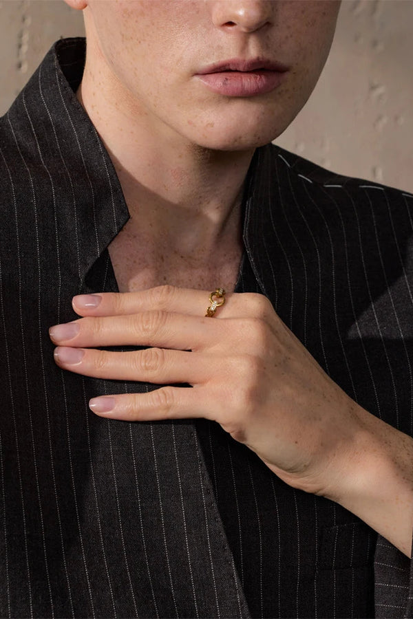 Person wearing a black pinstripe suit with a gold ring on a neutral background