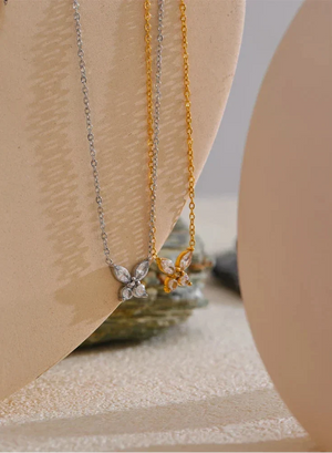 Two butterfly-shaped necklaces on a beige stand with a neutral background