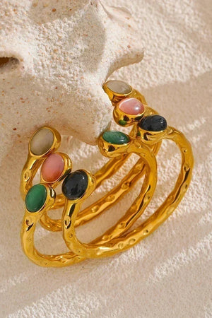 Gold ring with colorful gemstones on a textured beige surface