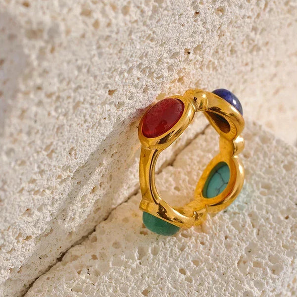 Gold-plated ring with red, green, and blue gemstones on textured stone background