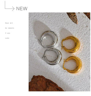 Two pairs of hoop earrings, one silver and one gold, on a textured white surface with a quote.