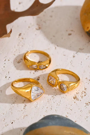 Three gold rings with gemstones on a textured surface