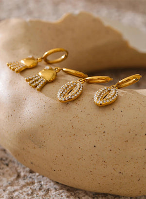 Gold earrings with gemstones on a textured beige surface