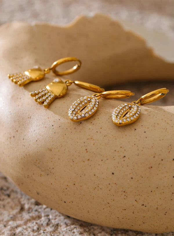 Gold earrings with gemstones on a textured beige surface
