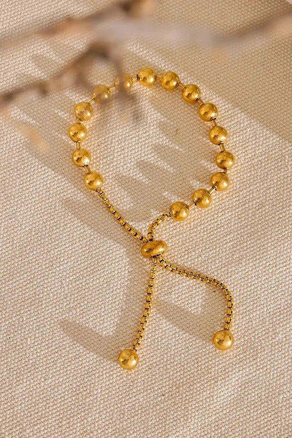 Gold beaded bracelet on a beige fabric background.