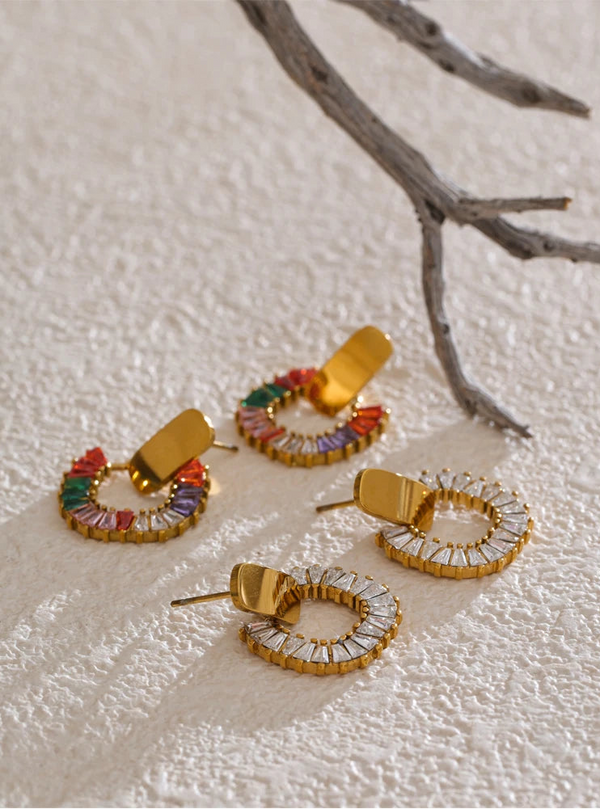 Set of gold hoop earrings with colorful gemstones on a textured surface.