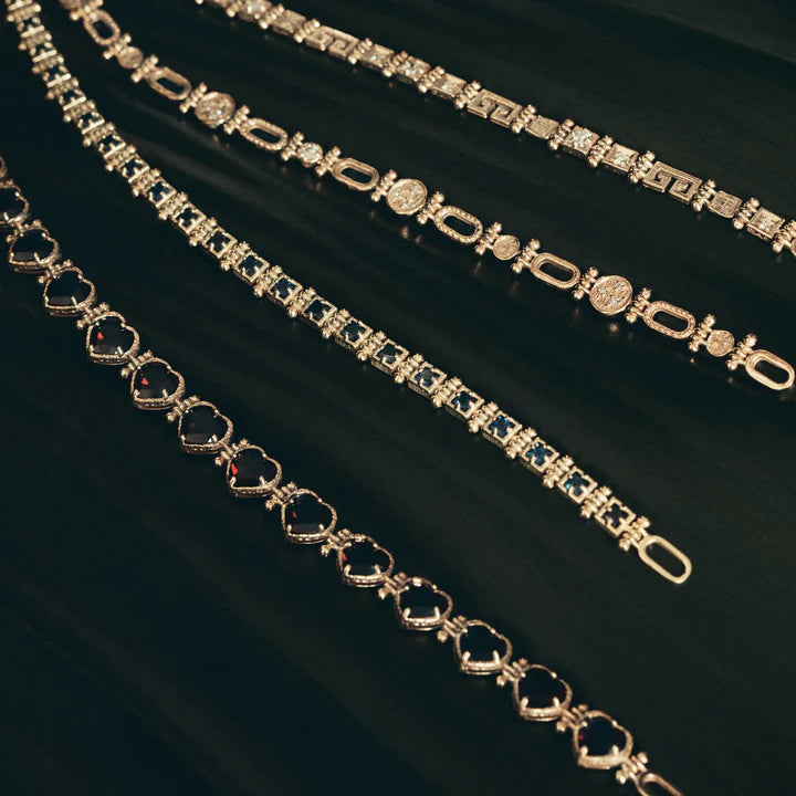 Two gold bracelets with gemstones on a dark fabric background