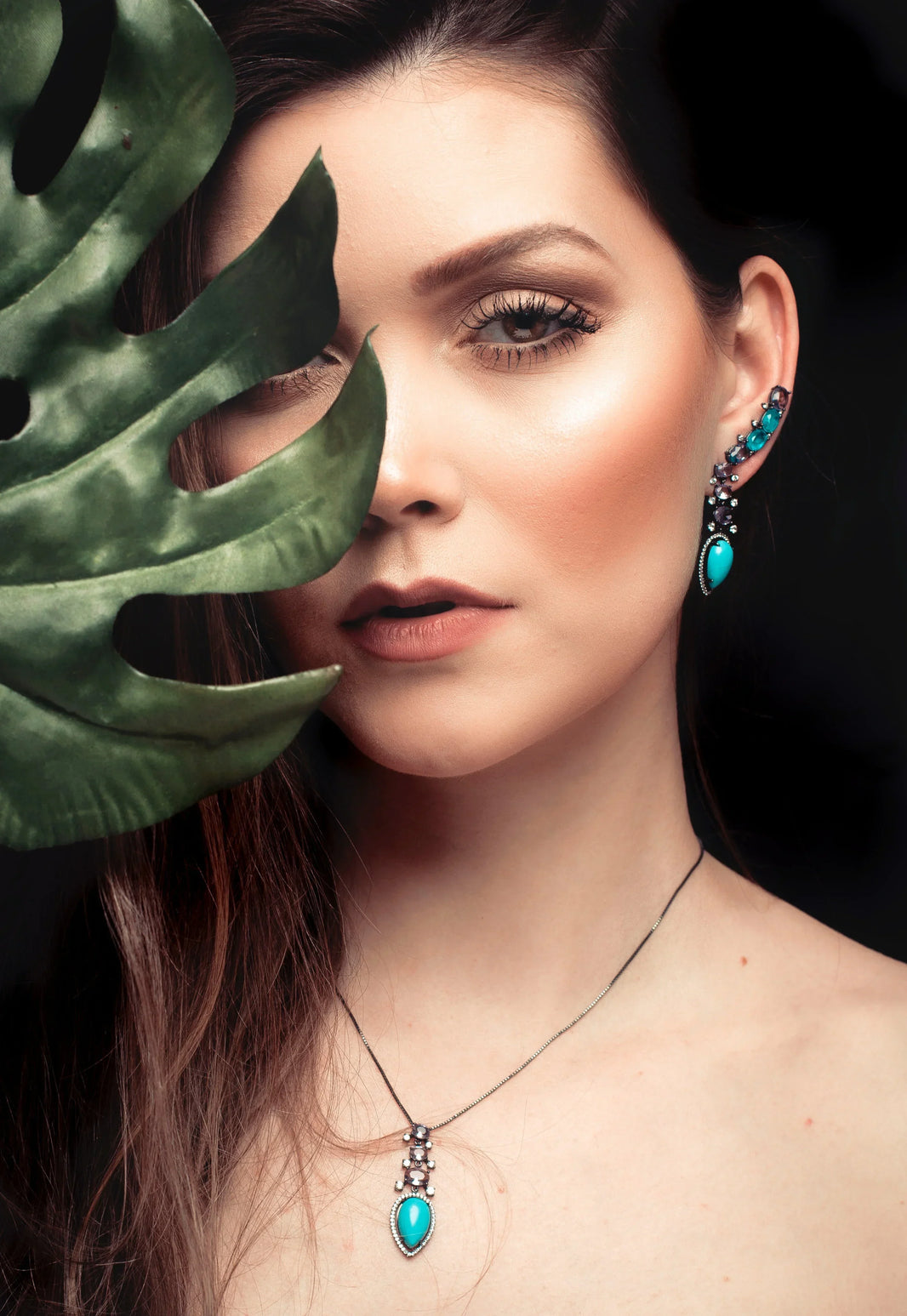Woman wearing turquoise jewelry with a leaf in front of her face