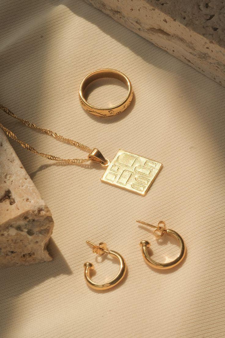 18K gold-plated hoop earrings, pendant necklace, and ring on stone background – TM & Co Jewels