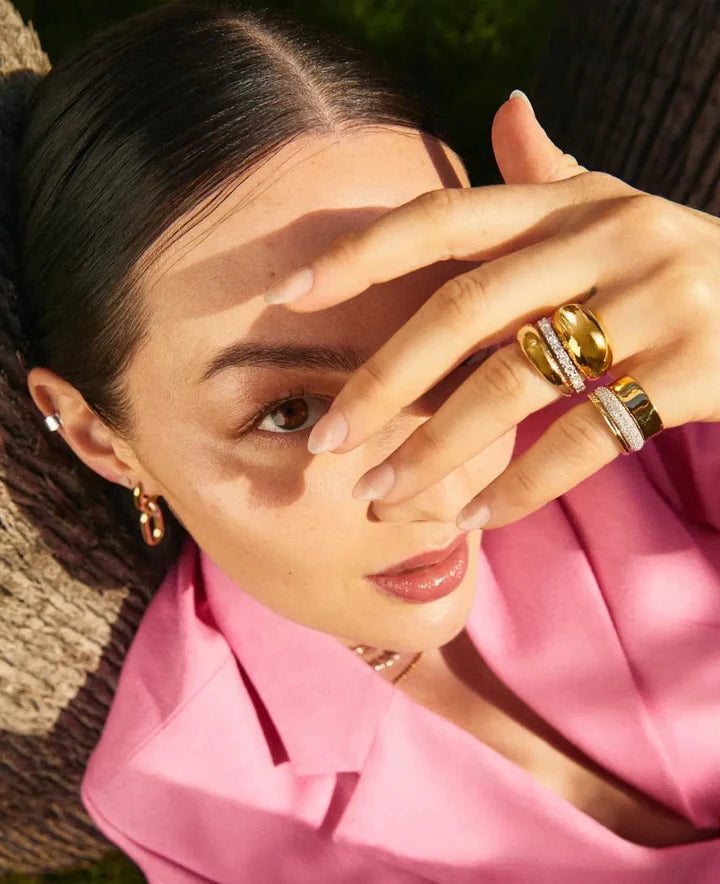 Woman wearing gold jewelry with a pink top, outdoors.