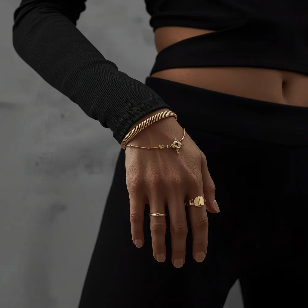 Hand wearing gold bracelets and rings against a dark background