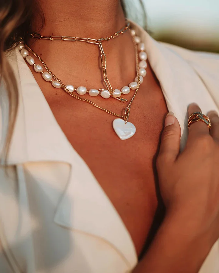 Close-up of layered pearl and gold necklaces with a hand wearing a ring.