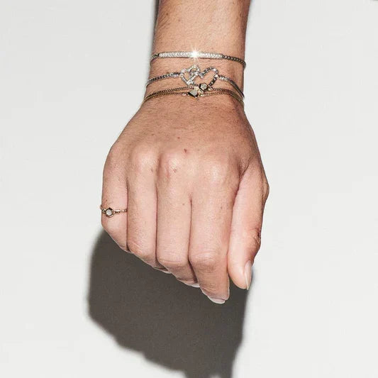 A close-up of a delicate bracelet stack featuring heart-shaped charms and fine gold chains from the TM & Co. Jewels collection