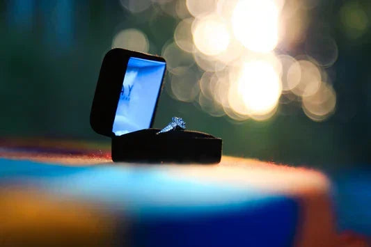 A quality-crafted diamond engagement ring displayed in a luxury box from the TM & Co. Jewels collection, set against a soft, bokeh background.
