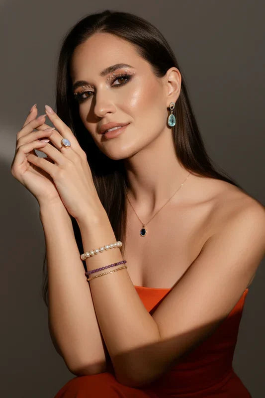 Woman wearing jewelry including earrings, a necklace, and bracelets against a brown background