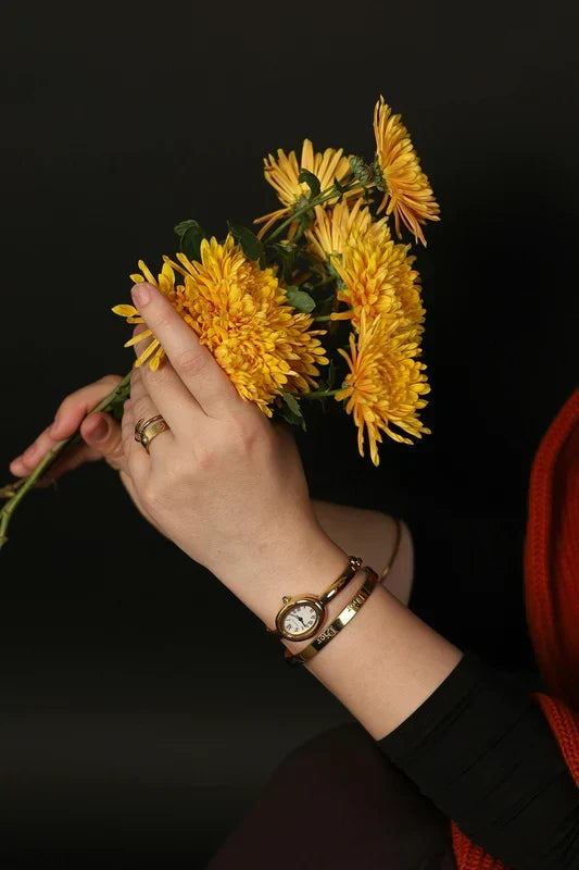 A quality-crafted minimalist watch and ring set from the TM & Co. Jewels collection, elegantly showcased with a bouquet of yellow flowers.