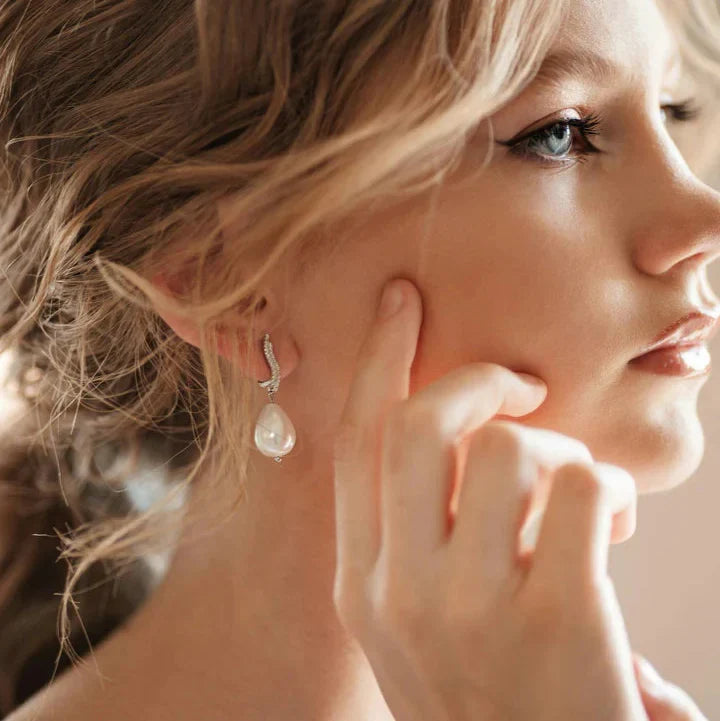 A close-up of a model wearing elegant pearl drop earrings from the TM & Co. Jewels collection, highlighting a refined and timeless aesthetic.