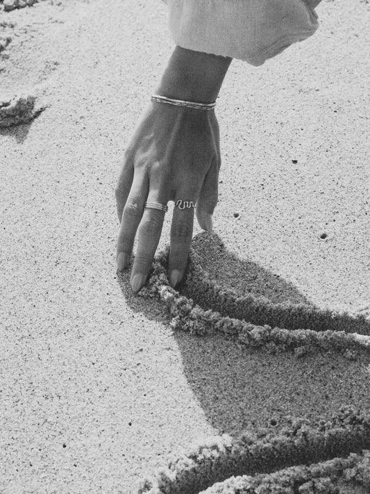 Hand with a ring touching sand, creating a pattern